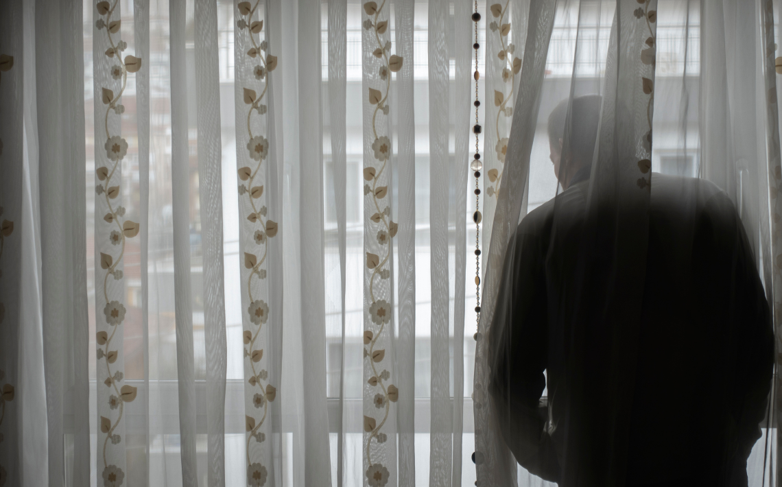 Adult looking out of window behind net curtains