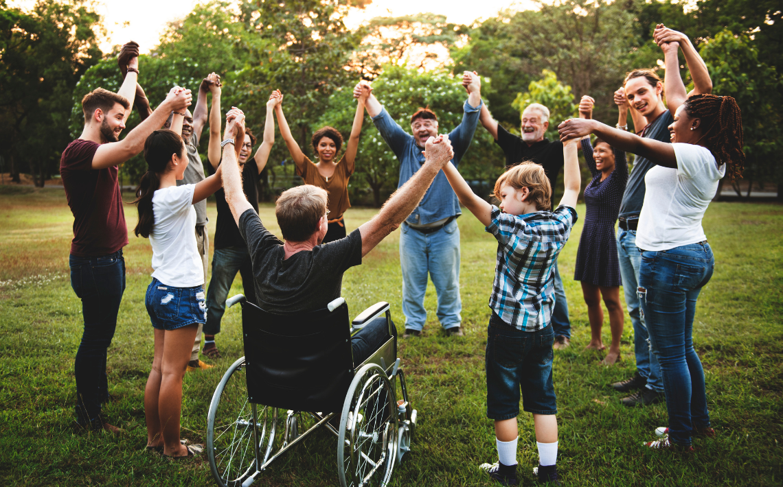 Group with man in wheelchair with arms in the air holding hands