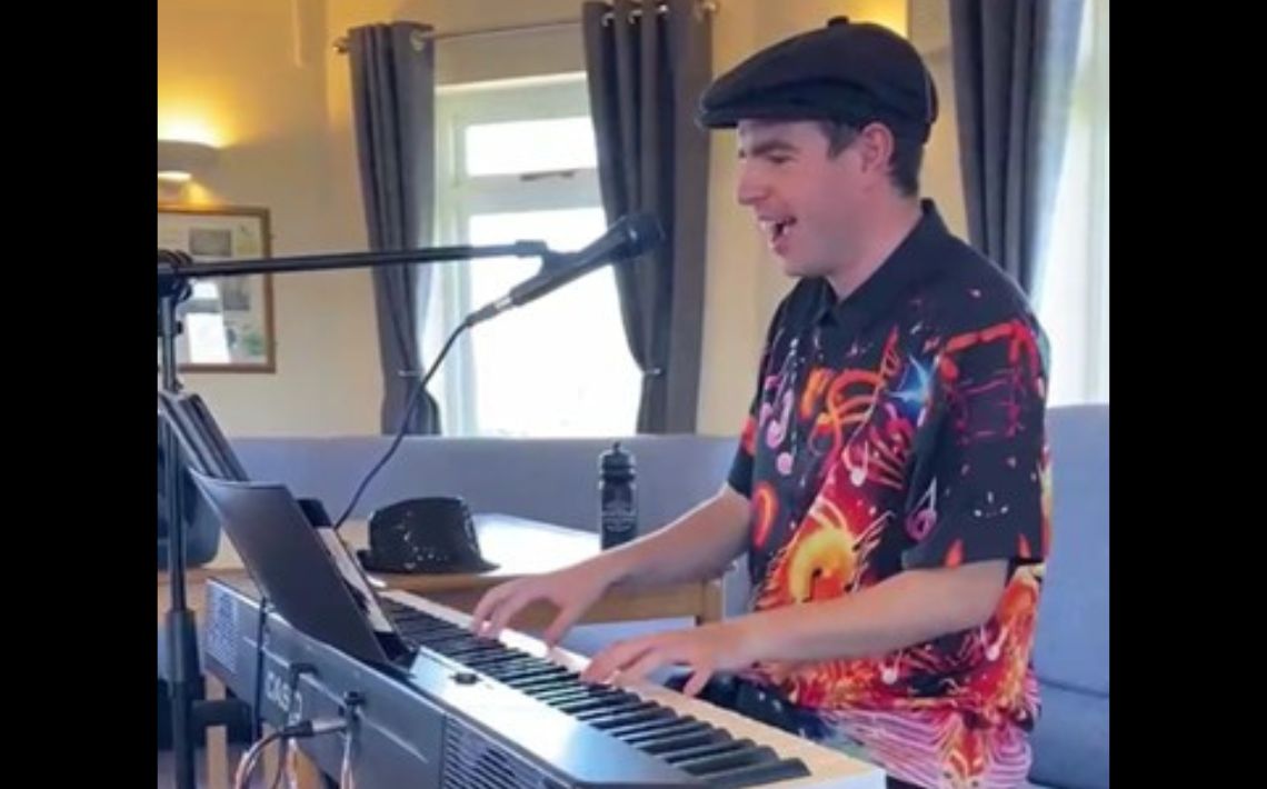 Young white male - wearing colourful shirt and flat cap, [playing the keyboard and smiling