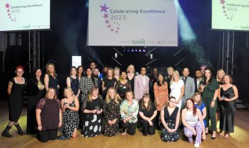 A large group of people stood and crouched in front of a screen displaying the text: Celebrating Excellence 2023.