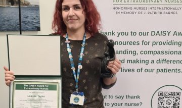 Photo of Leanne Taylor smiling, holding DAISY Award certificate and 