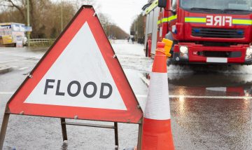 A flood warning sign blocking a flooded road with a fire engine.