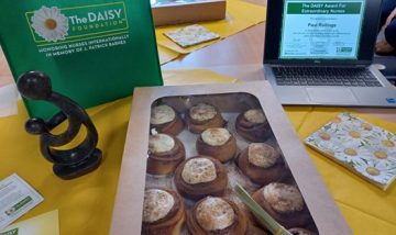 Photo of table with DAISY Award decorations, healer's touch sculpture, cinammon buns and laptop with Paul Rollings' certificate displayed