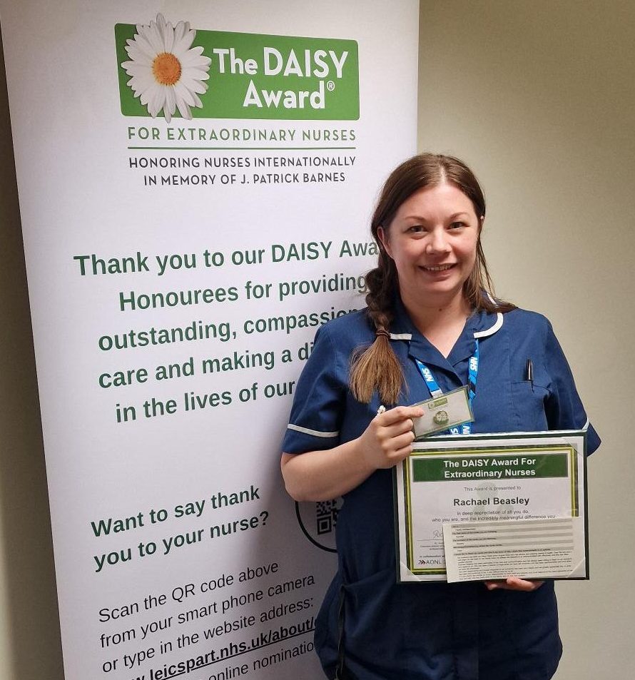 Photo of Rachael Beasley, smiling in her uniform, and holding DAISY Award certificate and pin badge