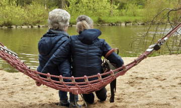 two women with grey hair sat on a hammock looking at the river