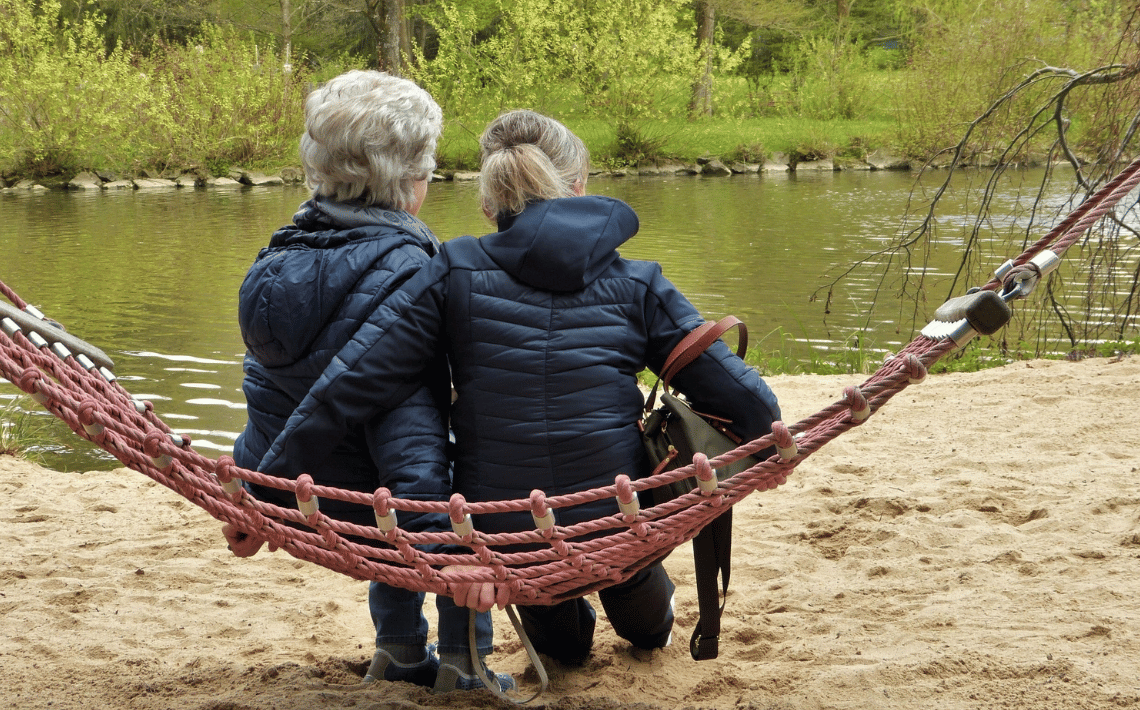 two women with grey hair sat on a hammock looking at the river