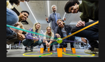 A mixed gender group of professional people doing a team building exercise with string, cup and ball