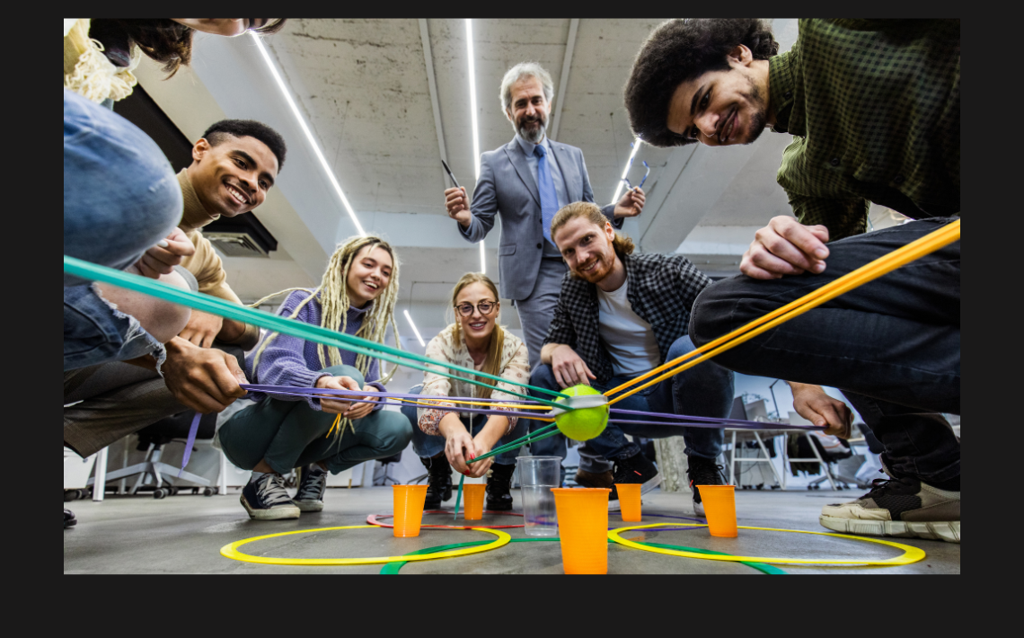 A mixed gender group of professional people doing a team building exercise with string, cup and ball