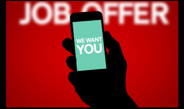Hand holding a phone with text saying: We want you. background text: Job offer