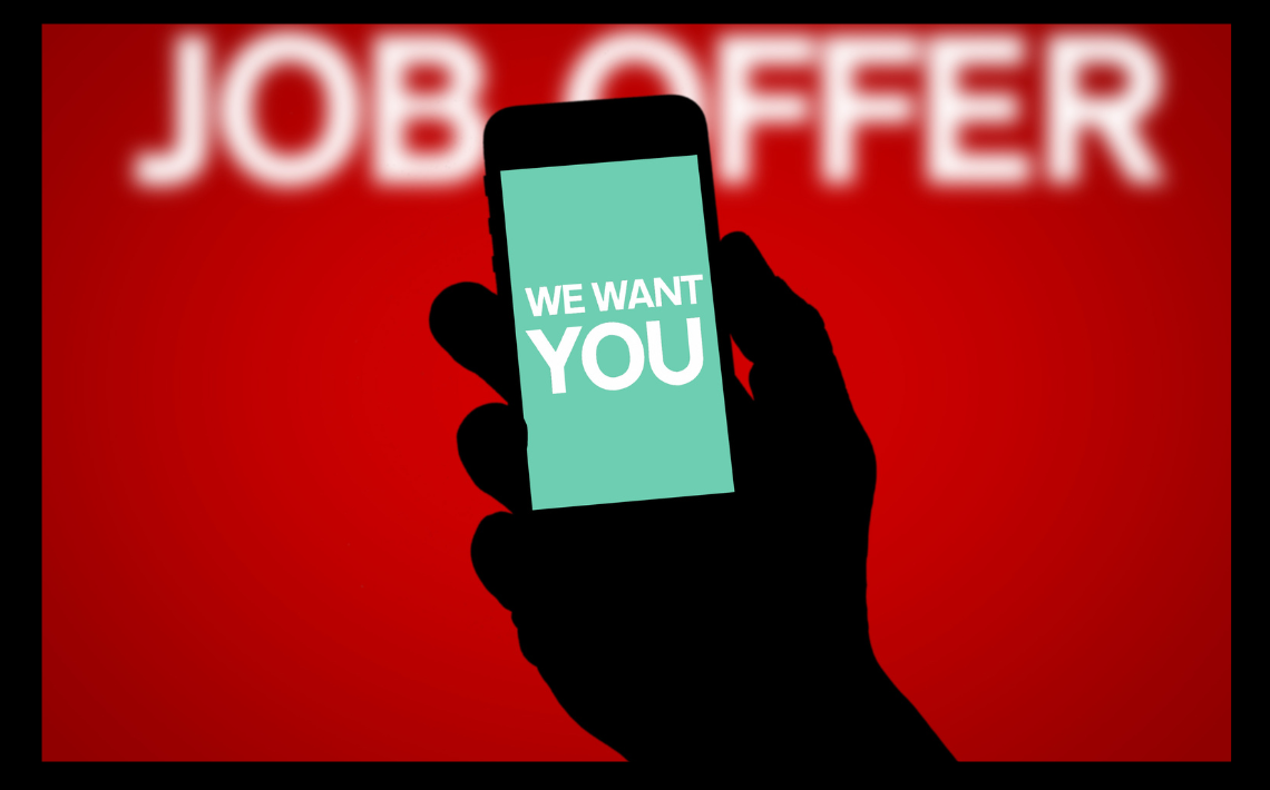 Hand holding a phone with text saying: We want you. background text: Job offer