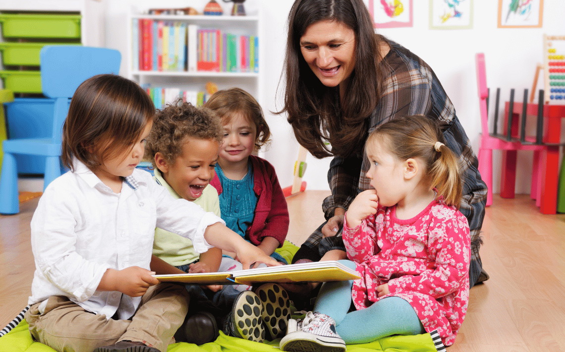 a group of pre-schoolers sit looking at a book with their teacher