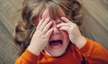 Toddler lying on floor with hands over face having a meltdown