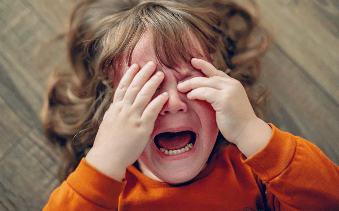 Toddler lying on floor with hands over face having a meltdown