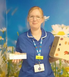 Nurse Heidi, wearing a blue uniform and holding some pressure ulcer props and resources, including a small, card skin tone tool