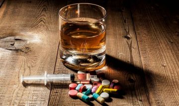 Glass of alcohol with syringe and drug tablets.