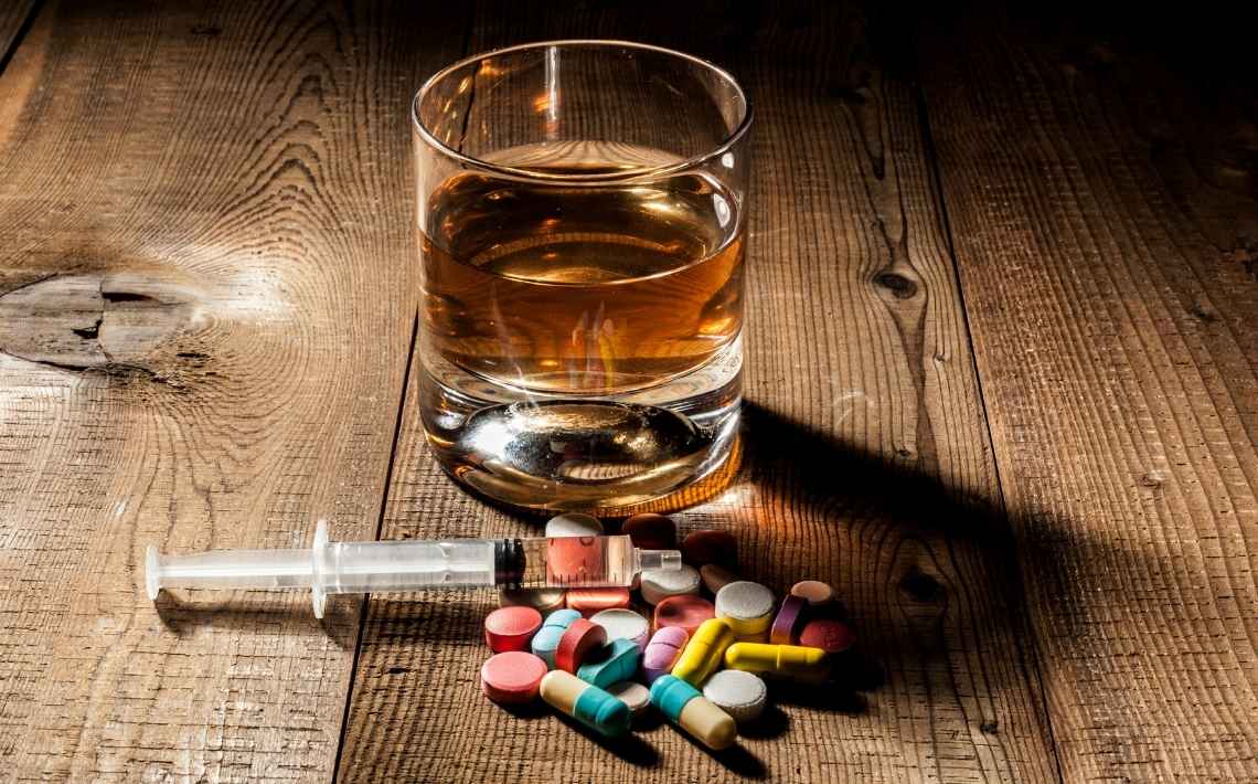 Glass of alcohol with syringe and drug tablets.