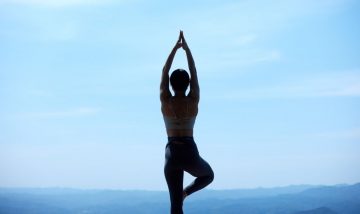 Silhouette of woman doing yoga pose with arms pointing upward