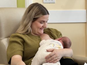 Smiling mum, Emily wears a green top and cuddles baby Marnie while feeding her following the frenotomy procedure