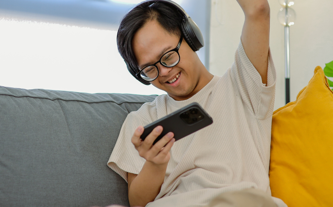 Child sat on a sofa playing on mobile device and raising arm up in celebration.