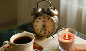 Cup of tea, alarm clock and lit candle light on a desk