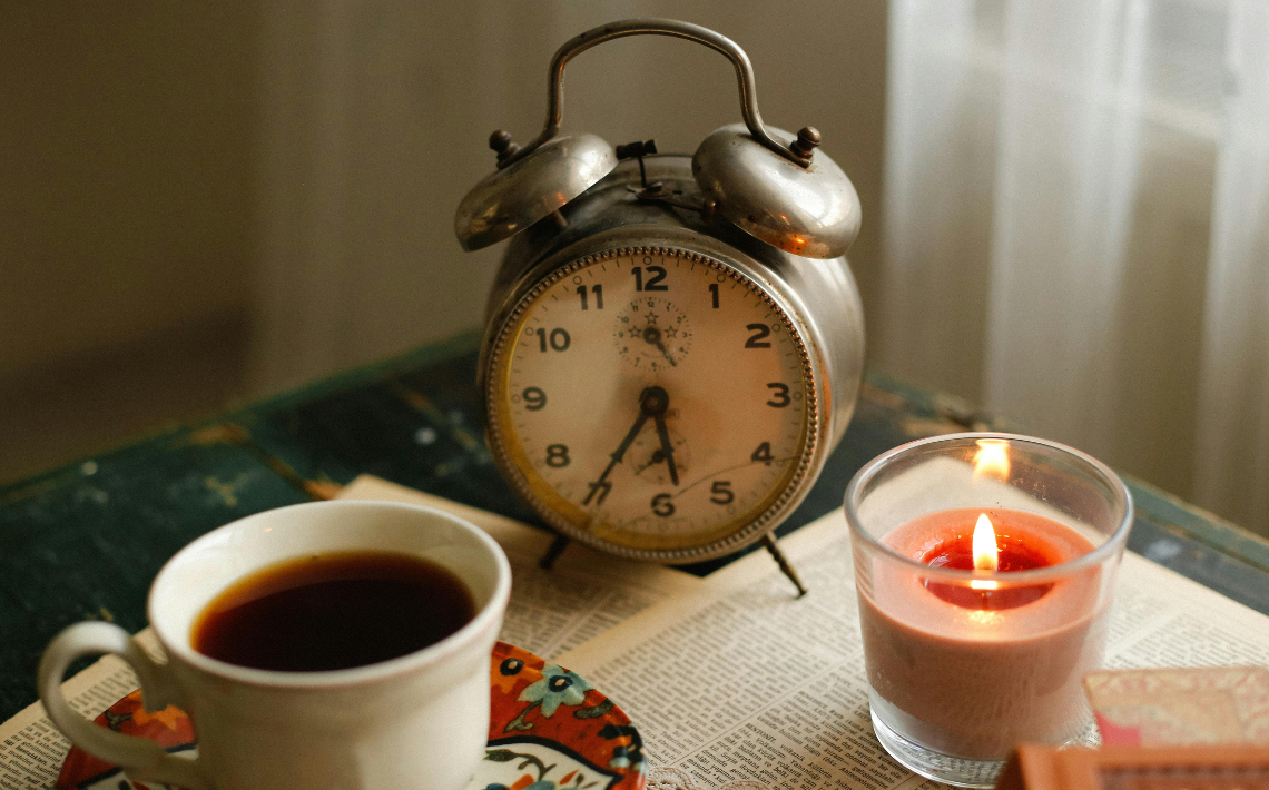 Cup of tea, alarm clock and lit candle light on a desk