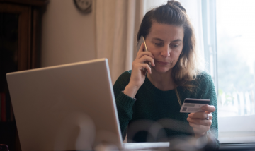 Woman on phone call in front of laptop holding credit card