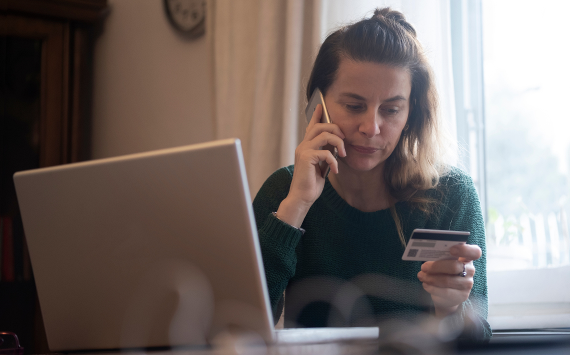 Woman on phone call in front of laptop holding credit card
