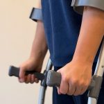 Person walking with a pair of crutches. Focused on just the lower arm.
