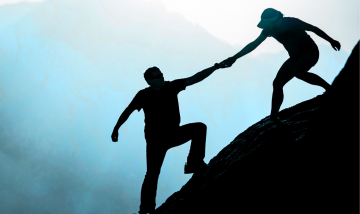 silhouettes of two people on mountainside - one person helping the other by pulling them by the hand