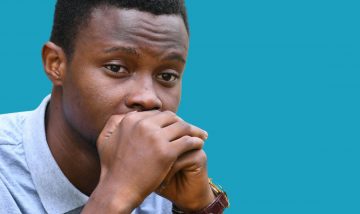 young black man with hands over mouth looking anxious and distant
