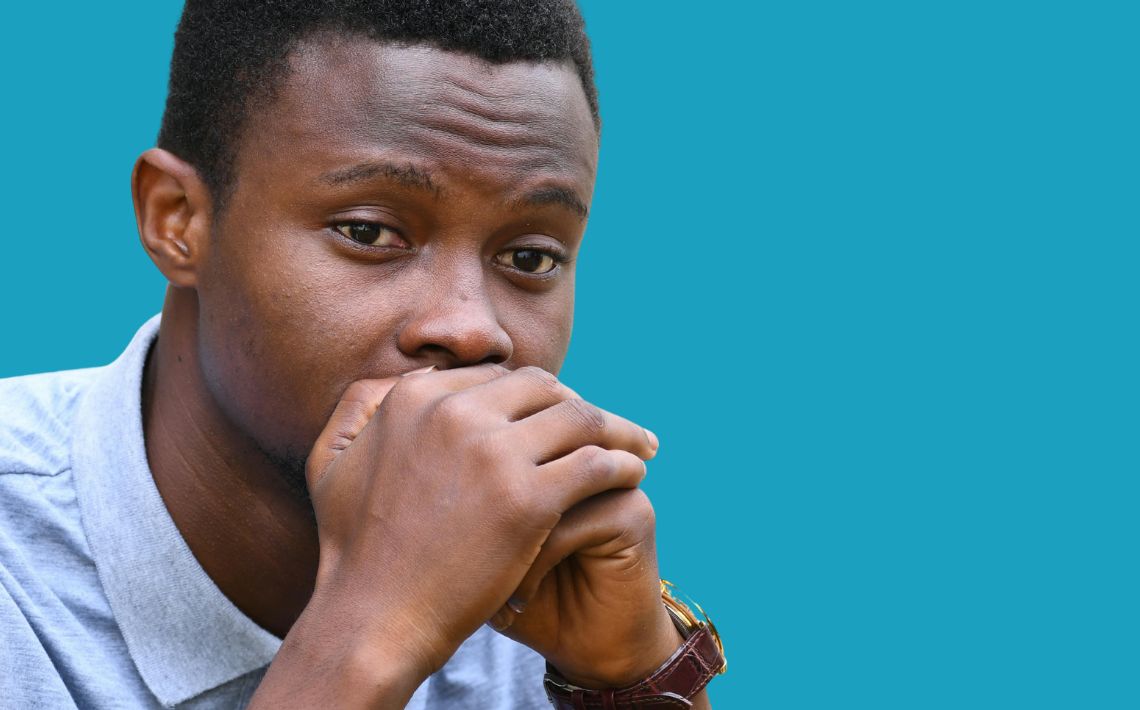 young black man with hands over mouth looking anxious and distant