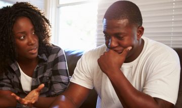 Young back couple - woman on left, man on right. Man looks worried. Woman appears to reassure him.
