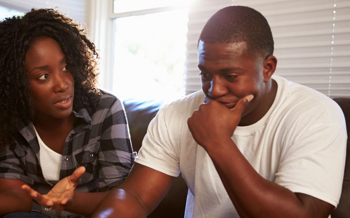 Young back couple - woman on left, man on right. Man looks worried. Woman appears to reassure him.