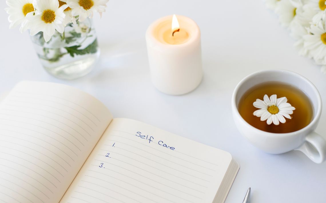 self care items including flowers candle, cup of tea and a note book