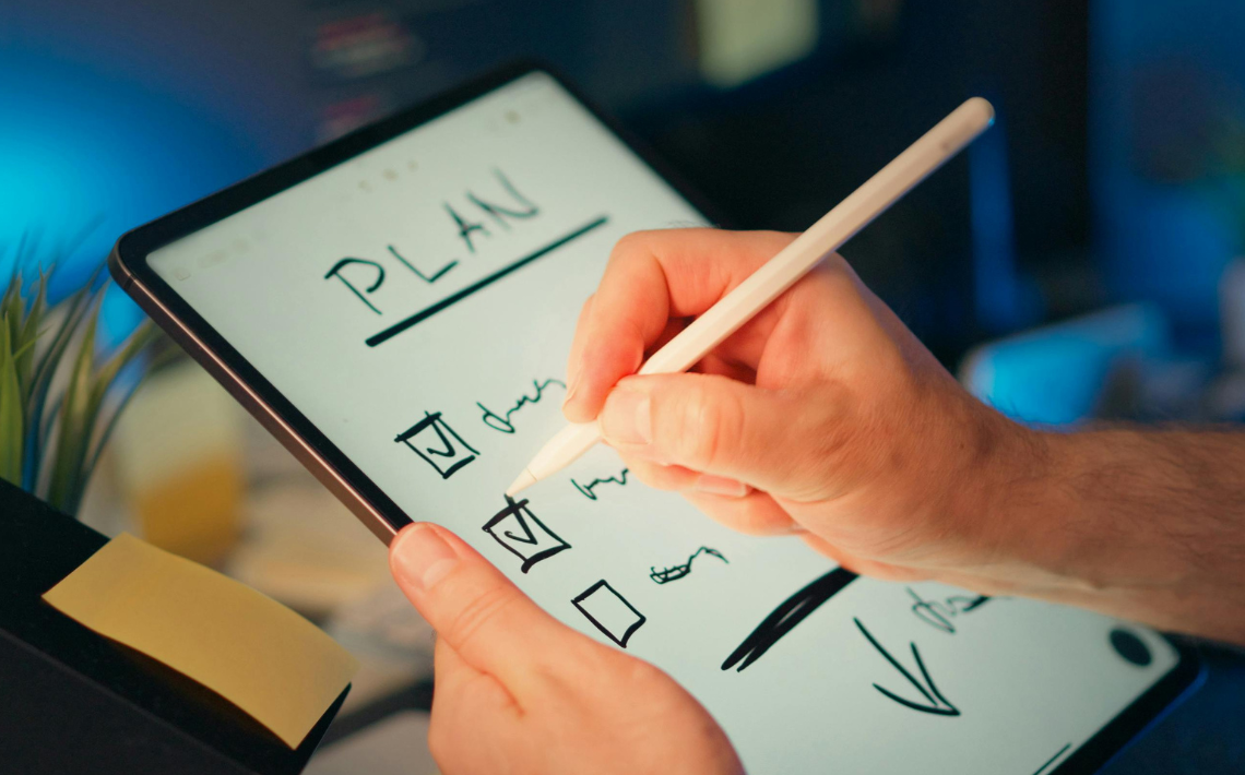 Hand held white board with 'Plan' tick list. Person's had shown ticking an item
